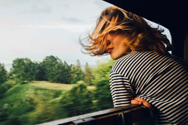 Blonde Frau fährt mit der Bahn und streckt ihren Kopf aus dem Fenster, ihre Haare wehen im Wind