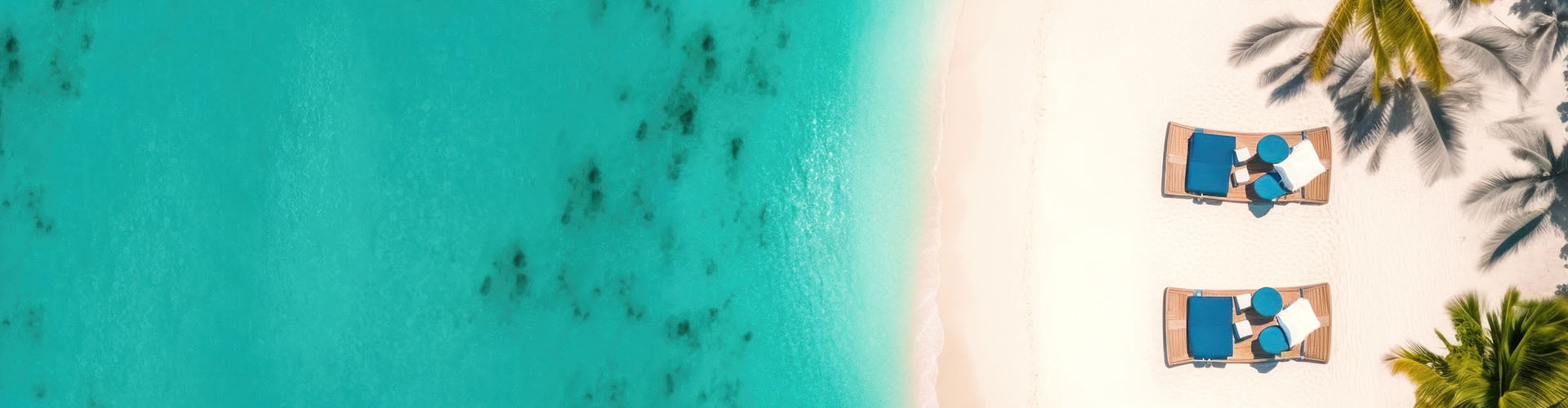 Sommerurlaub: Türkisblaues Meerwasser und weisser Sandstrand, Palmen und zwei bequeme Liegen laden zum Verweilen ein