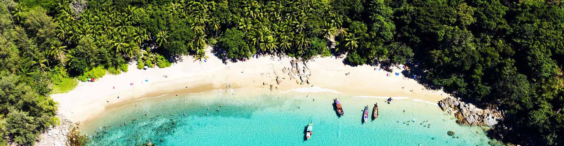 Tropischer Sandstrand mit türkisblauem Meer, Palmen und Booten aus der Luft betrachtet