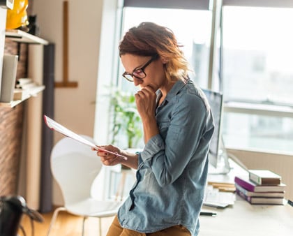 Frau mit Brille, liest sich Dokumente durch und überlegt, ob eine Reise storniert werden soll