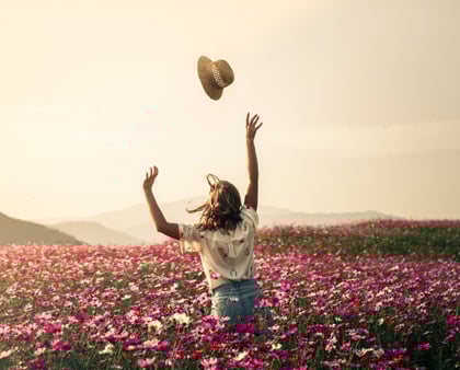 Frau in einem Blumenfeld, wirft ihren Hut in die Luft, gut geschützt im Falle einer Reisestornierung