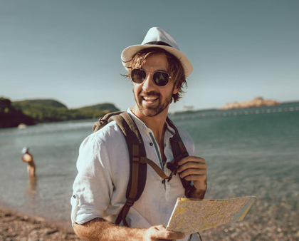 Mann mit Hut und Sonnenbrille, Urlaub am Strand, mit einer Reisekarte in der Hand