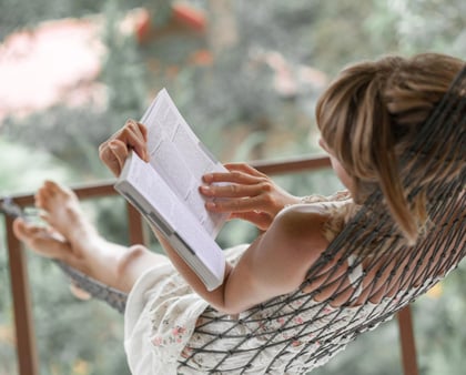 Eine Frau, in der Hängematte sitzend, liest ein Buch während der Ferien und Feiertage