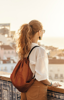 Eine Frau mit Rucksack blickt von einem Aussichtspunkt auf eine Stadt hinunter