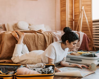 Frau liegt am Boden in der Wohnung, packt ihre Koffer und studiert die Reisekarte