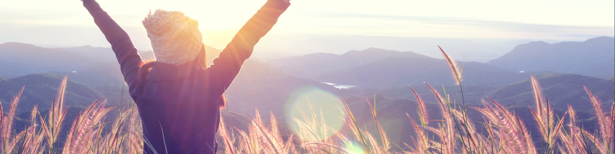 Rückenansicht einer Frau mit Haube im Frühling, auf einem Feld stehend, genießt den Sonnenaufgang