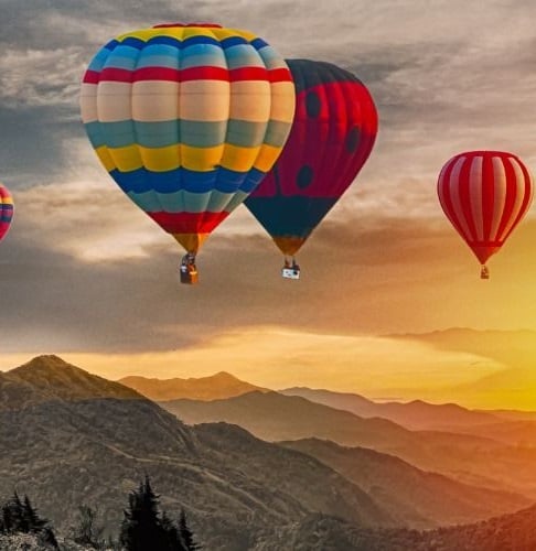 Ansicht von Bergen bei Sonnenuntergang, drei bunte Heißluftballons schweben darüber