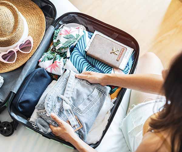 Offener Reisekoffer mit Kleidung, Reisepass und Reiseutensilien beim Packen für den Urlaub