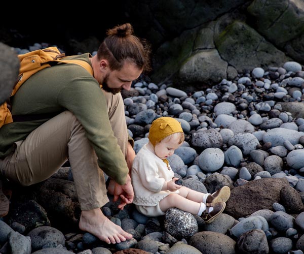 Vater mit Rucksack und Baby auf steinigem Strand