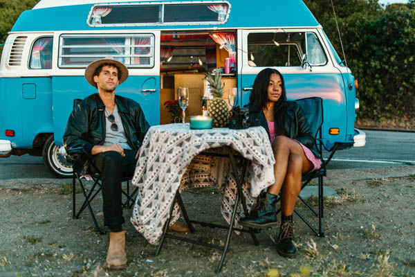 Pärchen sitzt am Tisch, vor einem blauen Camping Wagen
