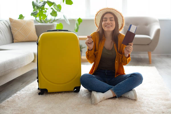 Frau sitzt auf dem Boden neben ihrem gelben Koffer und freut sich auf den Urlaub