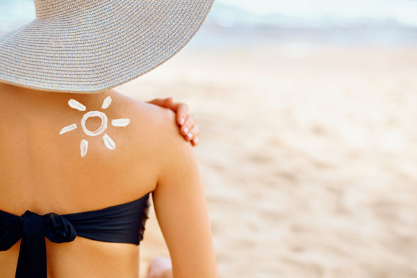 Rückenansicht einer Frau mit Sonnenhut, Sonnencreme ist in Form einer Sonne auf ihren Rücken aufgemalt