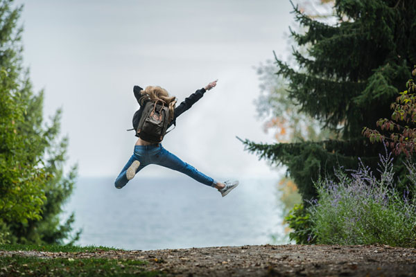Frau mit Rucksack springt in die Luft vor Freude