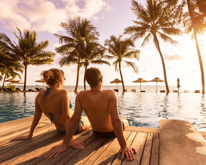 Pärchen am Pool mit Palmen, Reiseversicherungen für eine Auslandsreise