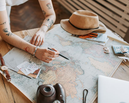 Reiseplanung, Hände die etwas auf einer Karte markieren, Reisepass, Sonnenhut und Kamera