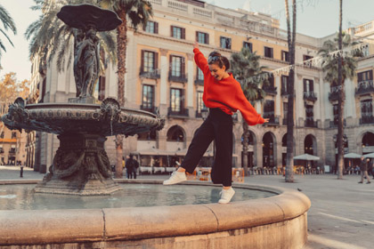 Frau in rotem Pullover balanciert auf einem Brunnen bei einer Städtreise
