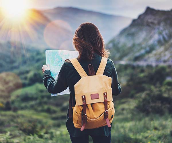 Rückenansicht einer Frau mit gelbem Rucksack, die eine Straßenkarte hält und in den Bergen unterwegs ist