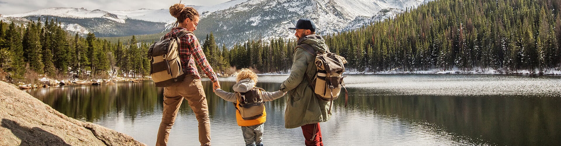 Familie mit einem Kind mit Rucksäcken an einem See während einer Bergwanderung.