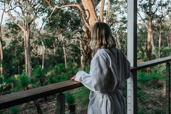 Frau blickt vom der Terrasse eines Hotels auf grünen Wald