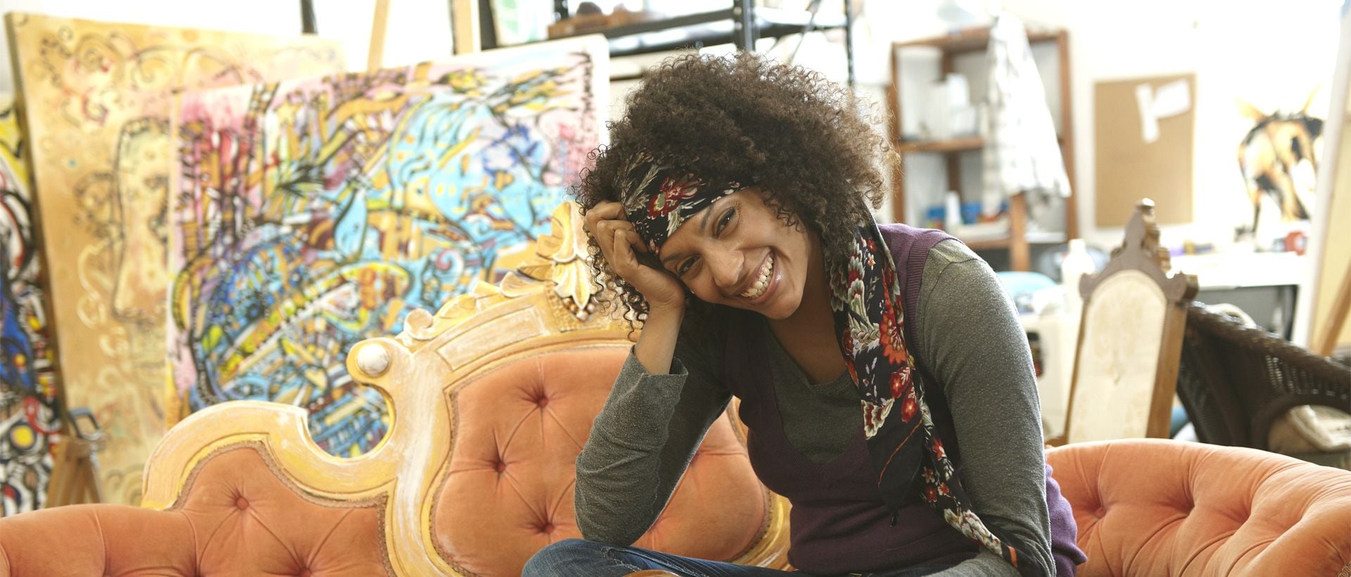 Frau mit lockigen Haaren die sich freut, auf einer Couch sitzend