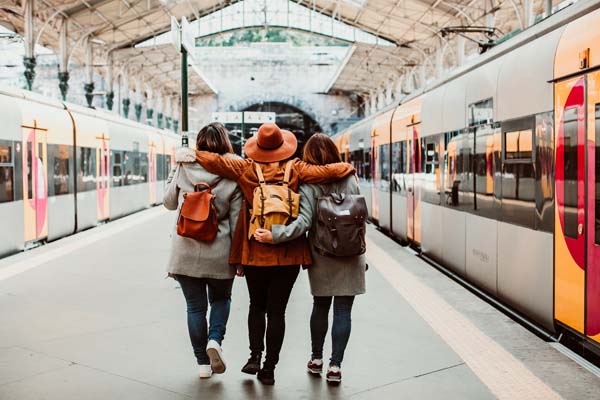Drei Freundinnen mit Rucksäcken umarmen sich am Bahnhof
