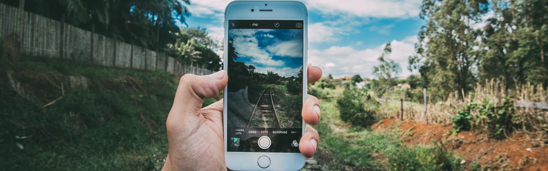 Hand hält Smartphone, Natur und Bahngleise im Hintergrund