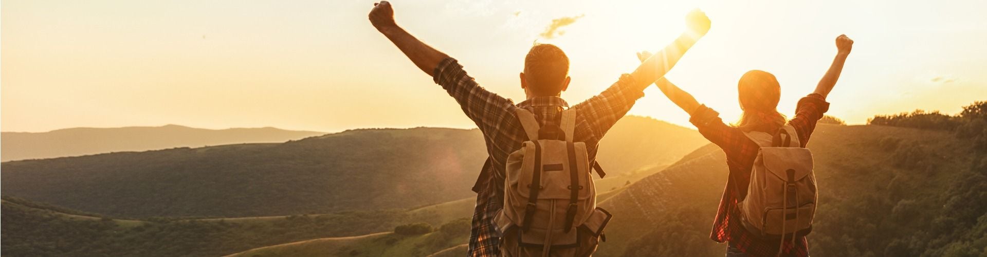Mann und Frau mit Rucksäcken, strecken die Arme in die Luft und genießen die Berge