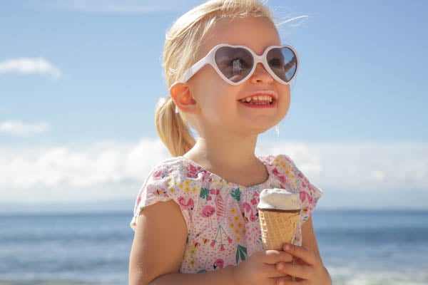 Blondes Mädchen am Strand, mit Herz-Sonnenbrille und ein Eis in der Hand