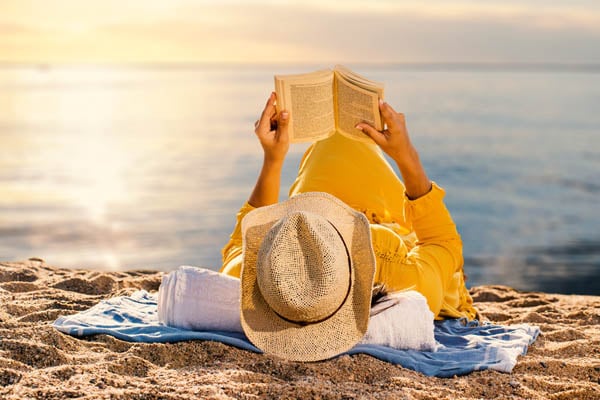 Frau liegt entspannt am Strand und liest ein Buch
