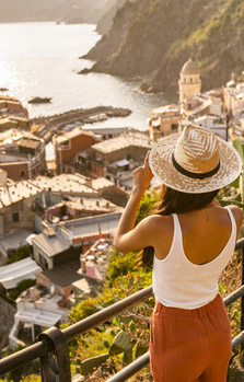 Frau mit Sonnenhut auf Auslandsreise, fotografiert Ausblick über Küstenstadt, gut versichert mit einer Auslandskrankenversicherung