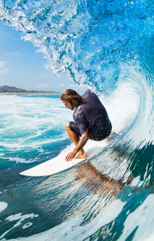 Mann mit einem Surfbrett unter einer großen Welle, gut versichert mit dem Aktiv Schutz Paket