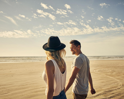 Frau mit Hut und lächelnder Mann im Urlaub am Strand