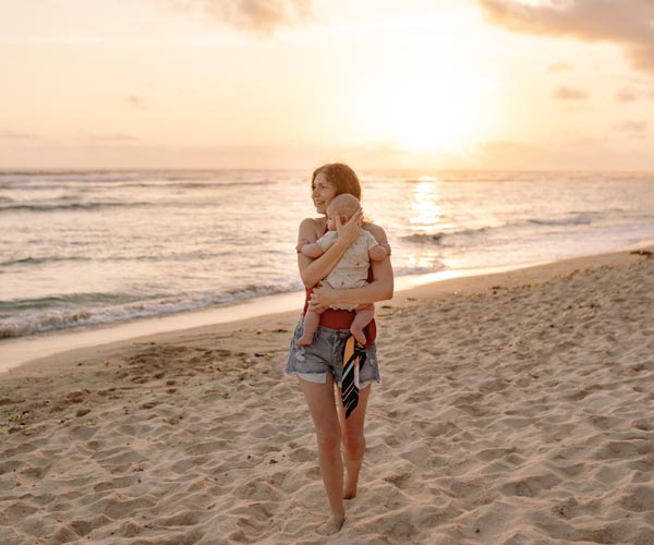 Frau mit Baby am Strand, im Hintergrund das Meer